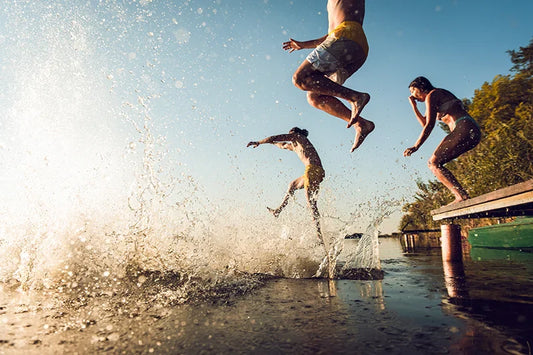 a group of friends jump off a platform into a lake